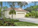 Home's yellow exterior features a tile roof, a two-car garage, and a paved driveway surrounded by lush landscaping at 7602 Partridge Street Cir, Bradenton, FL 34202