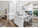 Island kitchen showcases white cabinets, stainless steel appliances, an island with bar seating and hardwood floors at 7317 Crape Myrtle Way, Sarasota, FL 34241