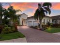 Beautiful home with a brick driveway, three-car garage, lush landscaping, and beautiful sunset at 7115 Callander Cv, Lakewood Ranch, FL 34202