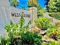 Westchester community entrance featuring stone signage, lush landscaping, and brick pillars, offering a welcoming first impression at 4825 Gulf Of Mexico Dr # 304, Longboat Key, FL 34228
