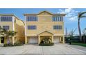 Exterior of a two-story, yellow townhouse with two garage doors, and a landscaped entrance at 653 Cedars Ct, Longboat Key, FL 34228
