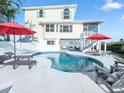 Backyard pool and deck with two-story home with balcony and red umbrellas at 114 Gull Dr, Anna Maria, FL 34216