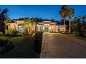 Elegant stucco home showcasing lush landscaping, palm trees, and a stately brick driveway at twilight at 3407 155Th E Ave, Parrish, FL 34219