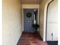 Inviting entryway with brick flooring and a gray front door adorned with a wreath and green plants at 1842 Country Meadows Ct, Sarasota, FL 34235