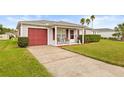 A well-maintained single-story home featuring a red garage door, and a neatly manicured lawn and driveway at 29353 Princeville Dr, San Antonio, FL 33576