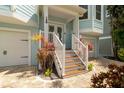 Inviting front entrance with decorative plants, a brick walkway, and white wooden stairs to a charming turquoise home at 130 50Th St, Holmes Beach, FL 34217