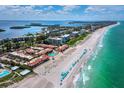 Expansive aerial view of condos along a pristine beach, complemented by inviting blue umbrellas and clear turquoise waters at 4621 Gulf Of Mexico Dr # 19B, Longboat Key, FL 34228