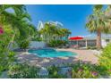 Inviting backyard pool surrounded by lush tropical landscaping and a red umbrella at 701 N Bay Blvd, Anna Maria, FL 34216