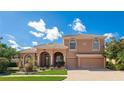 Beautiful two-story stucco home with a tile roof, arched entryway, and lush landscaping under a bright, partly cloudy sky at 6961 Scrub Jay Dr, Sarasota, FL 34241