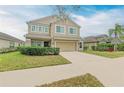 Two-story tan home featuring a well-manicured lawn, and a two-car garage at 11411 Flora Springs Dr, Riverview, FL 33579
