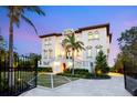 Elegant two-story home features an illuminated entry, terracotta roof, lush landscaping, and a secure gated driveway at 4205 Higel Ave, Sarasota, FL 34242