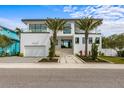 A modern two-story home with a white facade, balcony, and tropical landscaping at 7003 Holmes Blvd, Holmes Beach, FL 34217
