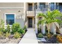 Close-up of the entrance to a condo unit with a small palm tree, black door and colorful landscaping at 23445 Collina Way # 10103, Port Charlotte, FL 33980