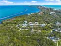 An aerial view showcasing a charming blue house surrounded by lush greenery and stunning ocean views at 691 Gulf Bay Rd, Longboat Key, FL 34228
