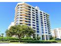 Stunning high-rise condo building featuring multiple balconies, lush landscaping, and a vibrant blue sky at 1211 Gulf Of Mexico Dr # 702, Longboat Key, FL 34228
