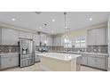 Modern kitchen with gray cabinets, stainless steel appliances, a large center island, and decorative tile backsplash at 11127 Devonbridge Dr, Palmetto, FL 34221