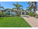 Beautiful single-story home with a brick driveway, lush landscaping, and large palm trees at 110 167Th E Blvd, Bradenton, FL 34212