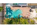 Aerial view of a pool area with a unique shape, brick patio, lounge chairs, and lush greenery at 4101 4Th Ave, Holmes Beach, FL 34217
