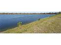 Panoramic water view showcasing a serene lakefront setting with grassy shoreline and neighborhood homes in the distance at 7036 Whittlebury Trl, Lakewood Ranch, FL 34202