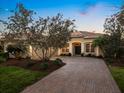 Inviting front of the home with a brick driveway, verdant lawn, and manicured shrubs under a blue sky at dusk at 7533 Trillium Blvd, Sarasota, FL 34241