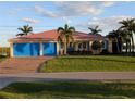 Charming home featuring a well-manicured lawn, a salmon-colored metal roof, and vibrant blue garage doors at 3572 Peace River Dr, Punta Gorda, FL 33983