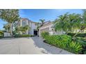 A beautifully landscaped home featuring a circular driveway, mature trees, and manicured shrubbery at 8025 Via Fiore, Sarasota, FL 34238