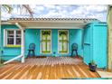 Inviting back porch features a wood deck, two chairs, and bright blue exterior walls with green trimmed doors at 256 144Th Ave, Madeira Beach, FL 33708