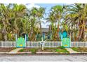 Bright blue home with palm trees, a white picket fence, and a whimsical gate featuring a sun design at 256 144Th Ave, Madeira Beach, FL 33708