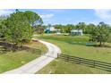Scenic view of a light blue home with mature trees, a long driveway, a lily pad pond, and a gated fence at 7677 Saddle Creek Trl, Sarasota, FL 34241