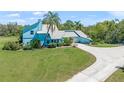 Light blue two-story home with a metal roof, lush green lawn, manicured bushes, and a concrete driveway at 7677 Saddle Creek Trl, Sarasota, FL 34241