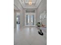 Bright foyer with white tiled floors, tray ceiling, chandelier, and double doors at 6620 35Th E Ct, Sarasota, FL 34243