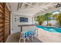 Outdoor bar area with a large TV for entertainment, views of the pool, and a tropical landscaped yard at 785 Jacaranda Rd, Anna Maria, FL 34216
