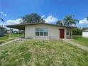 Exterior of a home with neutral paint, carport, small yard, and a bright red front door at 21114 Gladis Ave, Port Charlotte, FL 33952