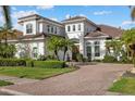 Elegant two-story home features white stucco, a tile roof, arched windows, and a paver driveway, surrounded by manicured landscaping at 125 12Th E Ave, Palmetto, FL 34221