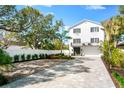 Beautiful two-story home featuring a balcony, pristine white stucco, gray brick driveway, and mature landscaping at 8258 Midnight Pass Rd, Sarasota, FL 34242