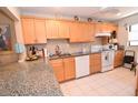 Well-lit kitchen featuring granite countertops, light wood cabinetry, white appliances, and tile flooring at 1601 Pelican Point Dr # Ha213, Sarasota, FL 34231