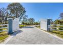 Welcoming entrance with a white gate and a paved driveway flanked by green grass and palm trees to the house at 9902 284Th St E E St, Myakka City, FL 34251