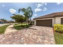 Charming home exterior featuring a well-maintained lawn, tile roof, and brick driveway under a sunny sky at 19993 Benissimo Dr, Venice, FL 34293