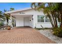 A well-kept exterior of the home shows a brick driveway and carport with a white facade and manicured tropical plants at 415 63Rd St, Holmes Beach, FL 34217