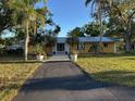 Yellow home with a metal roof, lush landscaping, and a paved walkway leading to the front door at 7036 Clark Rd, Sarasota, FL 34241