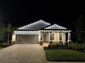 Charming home exterior featuring a paver driveway, garage, and manicured landscaping under soft, festive exterior lighting at 17676 Savory Mist Cir, Bradenton, FL 34211