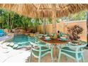 Outdoor dining area under tiki umbrella, with a view of the private pool and rock waterfall at 4001 5Th Ave, Holmes Beach, FL 34217
