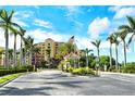 Community entrance with palm trees, meticulous landscaping, and guard house under a sunny blue sky at 611 Riviera Dunes Way # 107, Palmetto, FL 34221