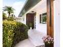 Close up of the front entry with a modern door, wood accents, and lush landscaping around the entryway at 2242 Sunnyside Ln, Sarasota, FL 34239