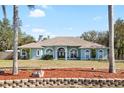 Charming light blue home featuring arched windows and mature landscaping against a clear blue sky at 12103 Shadow Run Blvd, Riverview, FL 33569