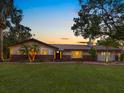 Inviting home exterior showcases a green lawn, palm trees, brick accents, and outdoor lighting at dusk at 6308 Caracara St, Sarasota, FL 34241