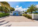 Charming blue bungalow featuring a brick driveway, white picket fence, and tropical landscaping at 113 Palm Ave, Anna Maria, FL 34216