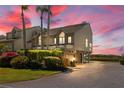 Coastal townhome features lush landscaping, brick paver driveway, and desirable under-house garage with sunset sky at 71 Tidy Island Blvd, Bradenton, FL 34210