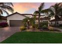 Beautiful one-story home featuring a three-car garage, brick-paved driveway, and lush tropical landscaping at sunset at 3814 Scrub Creek Run, Lakewood Ranch, FL 34211
