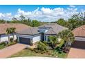 Landscaped single-story home with a tile roof, brick driveway, tropical plants, and an attached two-car garage at 5673 Piccolo St, Nokomis, FL 34275
